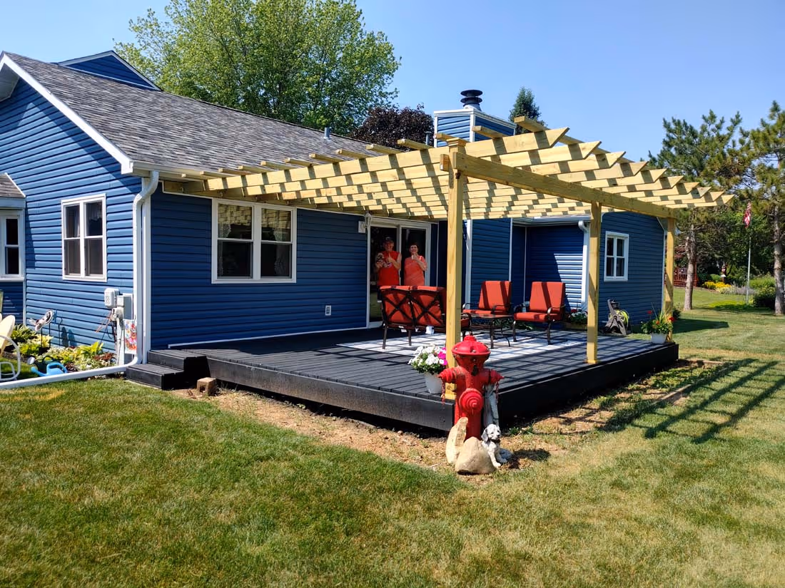 Blue house with a wooden pergola-covered patio featuring red chairs and a fire hydrant with decorative statues in the lawn.
