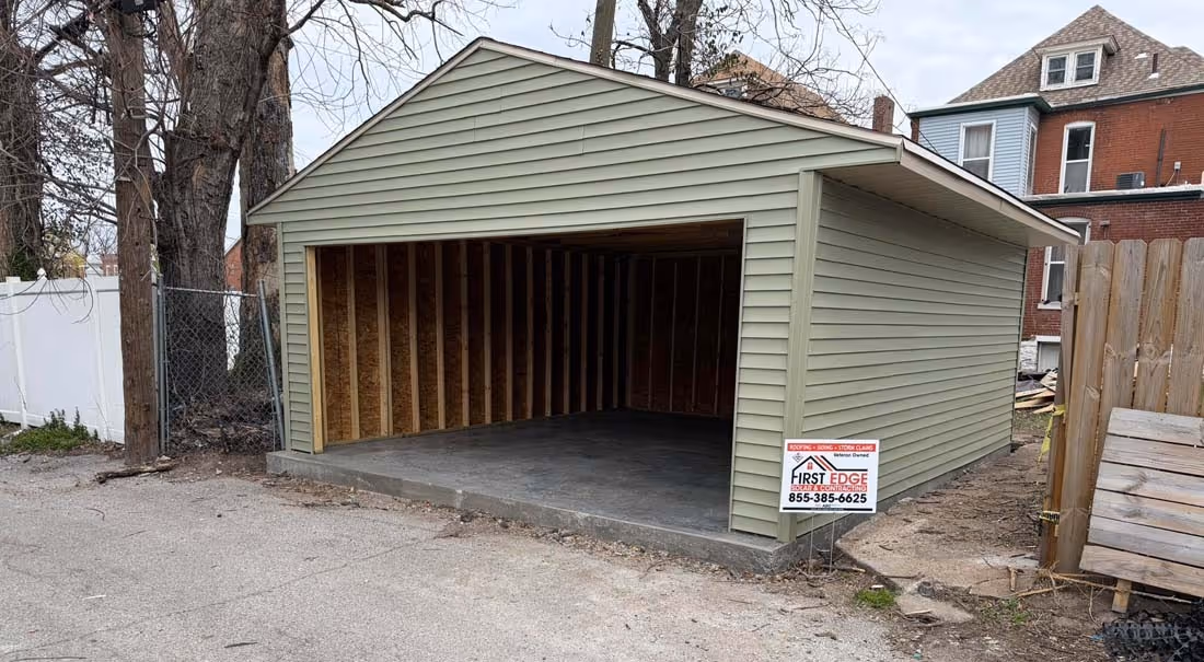 Newly constructed single-car garage with green siding and open interior showing wooden framing.